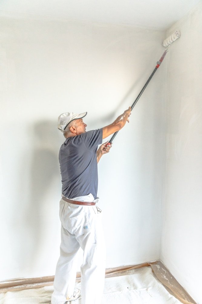 Senior,Man,Painting,A,White,Wall,,With,Paint,Roller,In