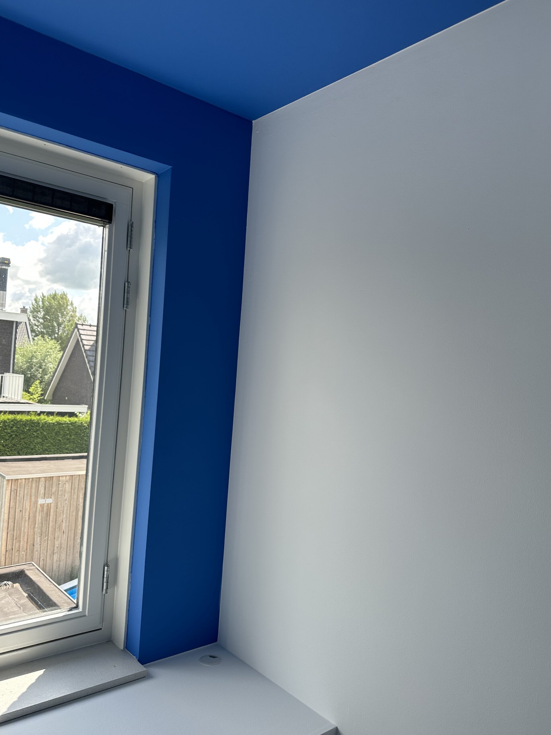 Blauwe binnenwand en witte raamhoek strak geschilderd
